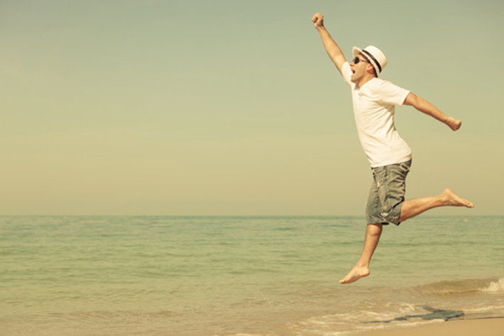 Giovane uomo felice che salta sulla spiaggia